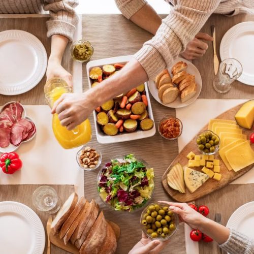 Aerial shot of a diverse brunch spread on a table with multiple hands serving food.