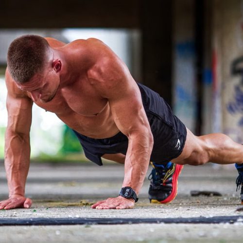 Shirtless caucasian man doing push-ups in an urban setting, showcasing strength and fitness.